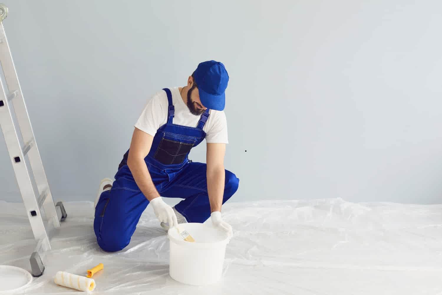 A painter in a white shirt and pants using a roller to paint a wall and ceiling, representing a professional painting service.